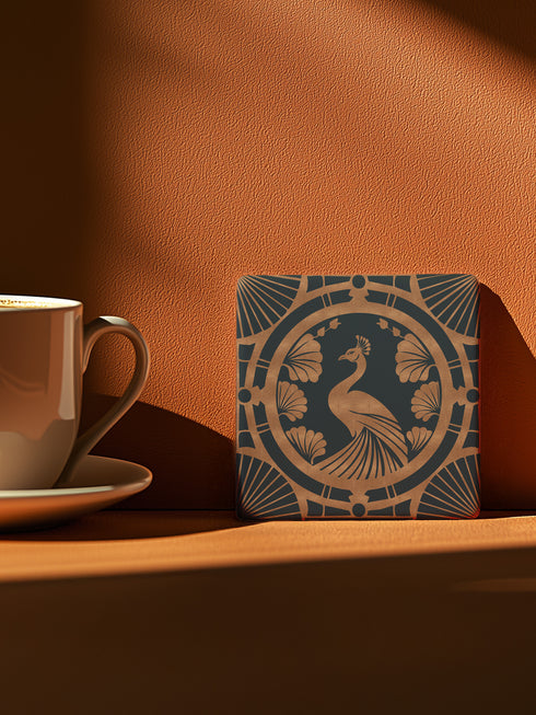 Square ceramic coaster featuring an Art Deco copper peacock design centered in a medallion, surrounded by fan patterns and shell motifs on a dark forest green background, with cork backing.
